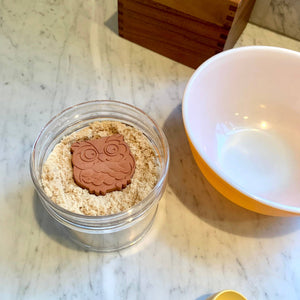 Jar of pet food with an owl-shaped cookie on a marble surface
