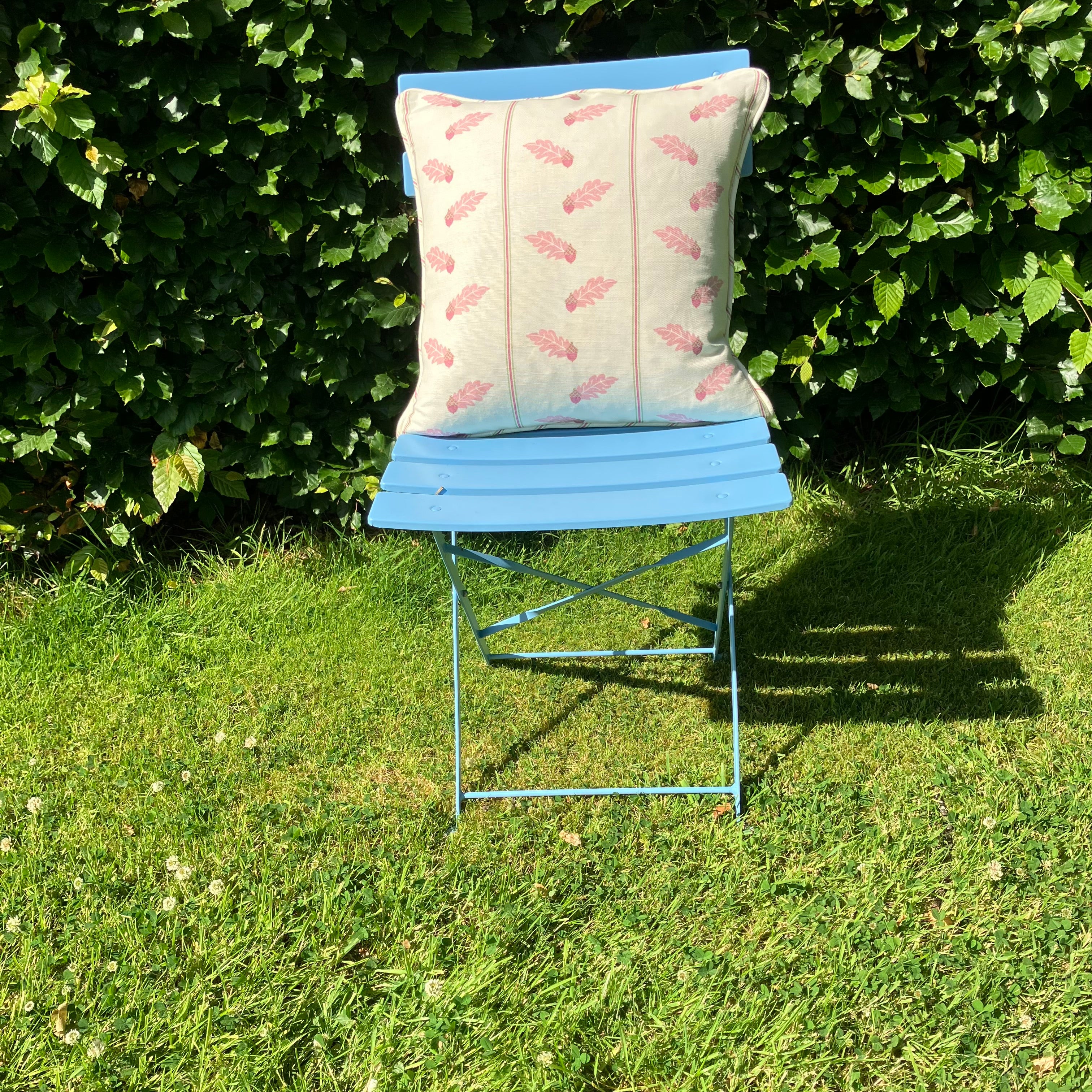  Pink cushion on blue chair on lawn in front of hedge