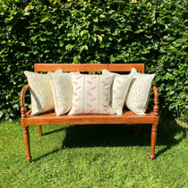 Five cushions on wooden bench  on lawn with hedge behind