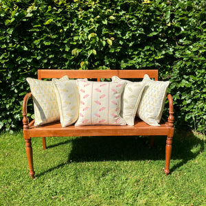Five cushions on wooden bench  on lawn with hedge behind