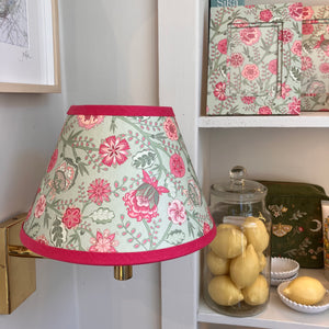 Pink and green lampshade on wall fitting with matching photo frame and Jar of lemons on shelf