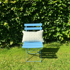 Blue chair with a cushion on grass against a green hedge