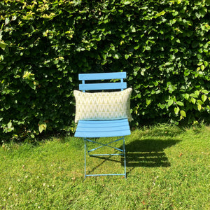 Blue chair with a patterned cushion against a green hedge
