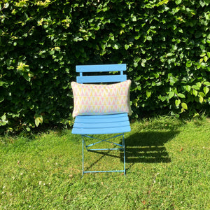 Blue chair with a patterned pillow against a green hedge